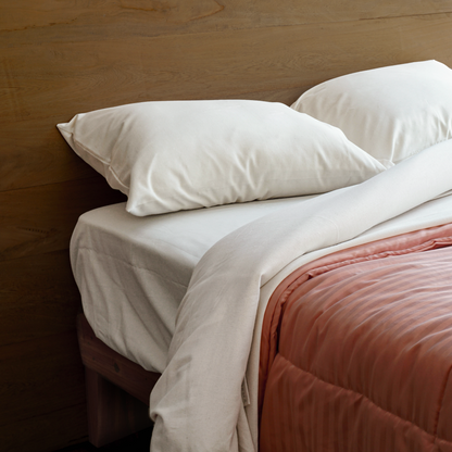 La imagen muestra una habitación con una cama a medio tender mostrando sus sabanas color blanco y almohadas del mismo tono.