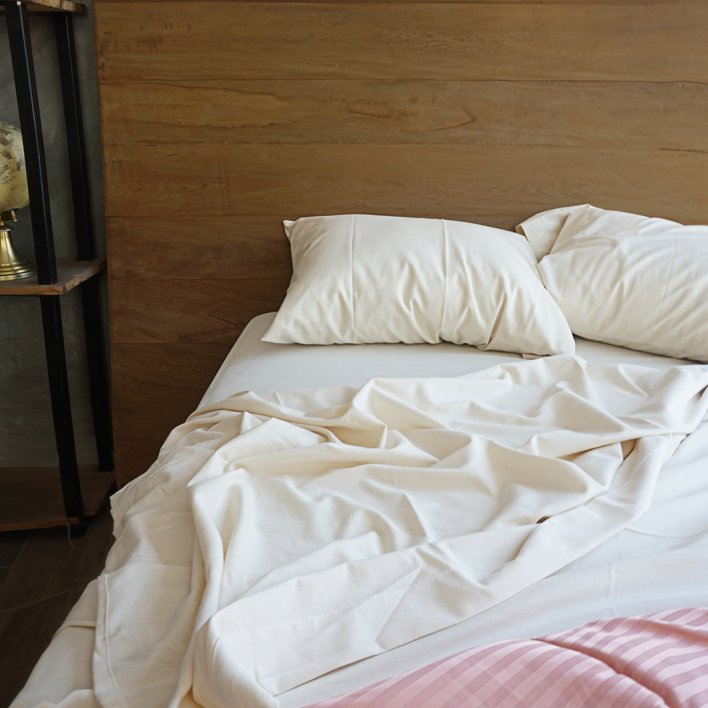 En una habitación se muestra una cama destendida luciendo unas sabanas y fundas decorativas para almohada de color natural.