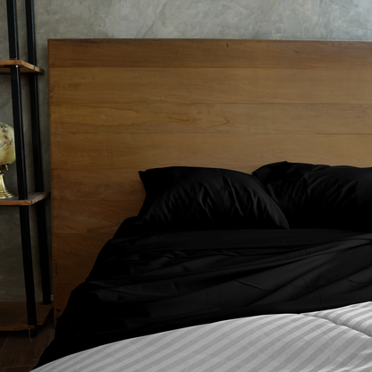 La imagen muestra una habitación y una cama la cual se encuentra vestida por un juego de sabanas y fundas decorativas para almohadas en color negro.