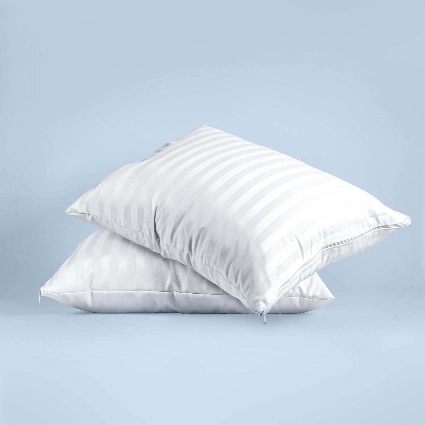 En un fondo azul se muestras dos almohadas una sobre en colores blancos con franjas satinadas. 
